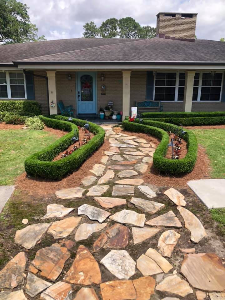 Charming stone walkway meandering through manicured, lush green hedges leading to a welcoming home entrance, crafted by Eric's Tidy Turf.