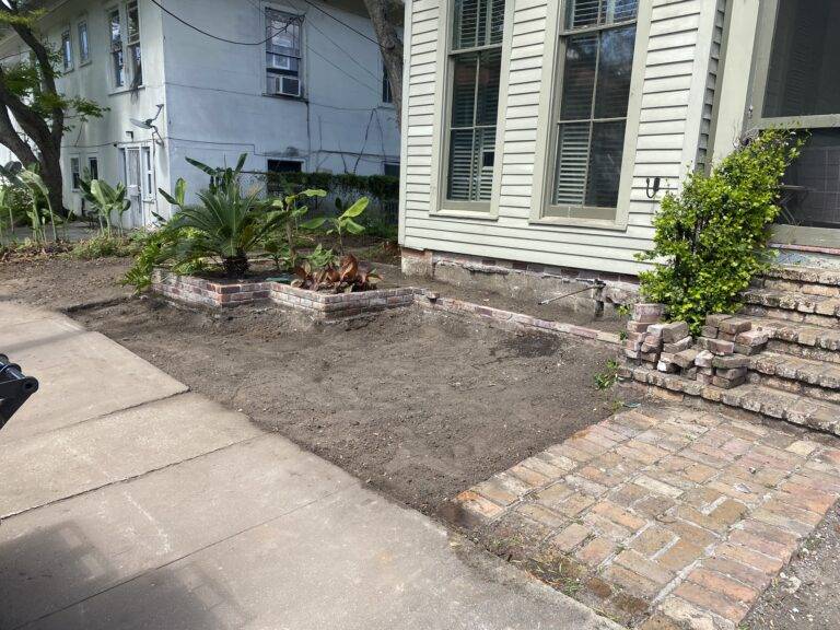 Beautifully landscaped front garden bed with vibrant purple foliage and green shrubs, framed by a brick border in front of a home, maintained by Eric's Tidy Turf.