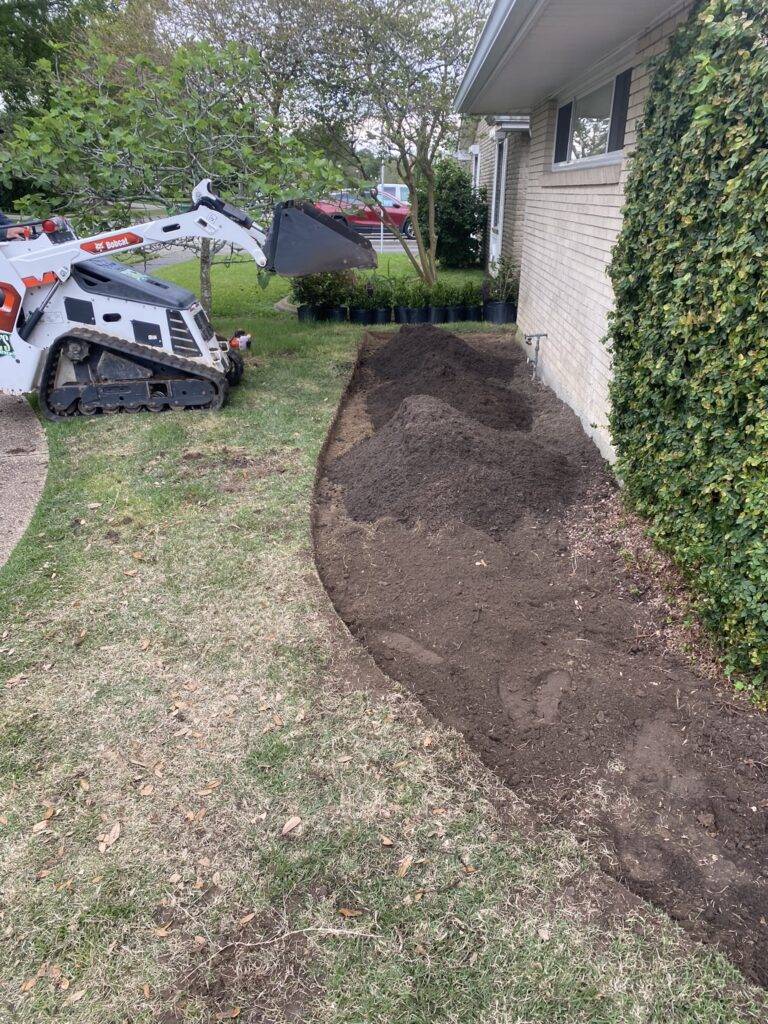 Beautifully landscaped front garden bed with vibrant purple foliage and green shrubs, framed by a brick border in front of a home, maintained by Eric's Tidy Turf.