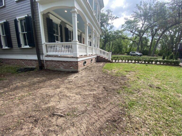 Beautifully landscaped front garden bed with vibrant purple foliage and green shrubs, framed by a brick border in front of a home, maintained by Eric's Tidy Turf.