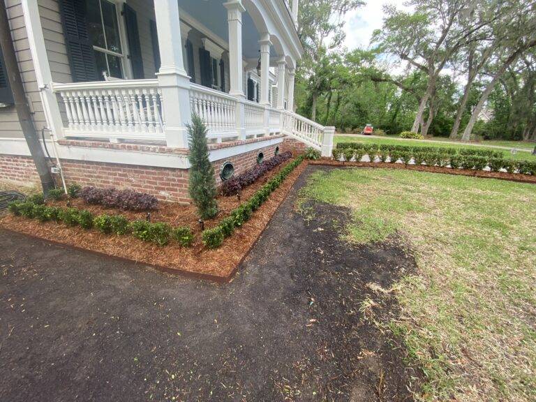 Beautifully landscaped front garden bed with vibrant purple foliage and green shrubs, framed by a brick border in front of a home, maintained by Eric's Tidy Turf.