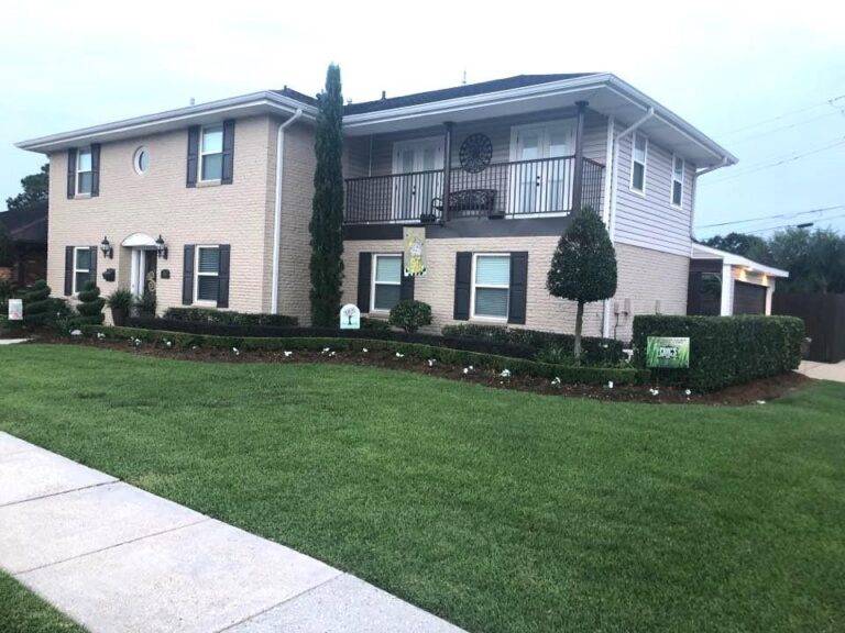 Beautifully landscaped front garden bed with vibrant purple foliage and green shrubs, framed by a brick border in front of a home, maintained by Eric's Tidy Turf.