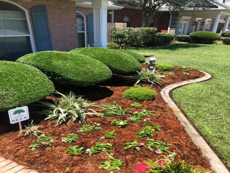 Beautifully landscaped front garden bed with vibrant purple foliage and green shrubs, framed by a brick border in front of a home, maintained by Eric's Tidy Turf.