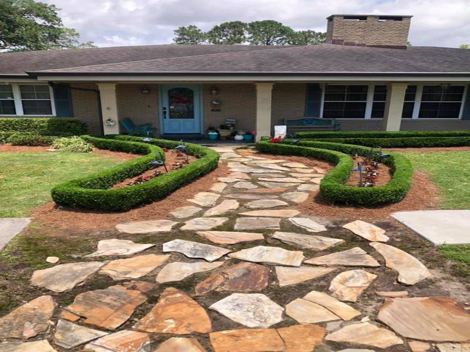 Beautifully landscaped front garden bed with vibrant purple foliage and green shrubs, framed by a brick border in front of a home, maintained by Eric's Tidy Turf.