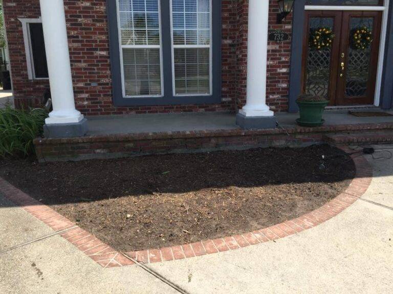 Prepared soil bed ready for planting within a brick-bordered garden space, at a residential home serviced by Eric's Tidy Turf.